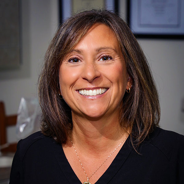 Smiling woman with shoulder-length brown hair wearing a black top in an office setting.