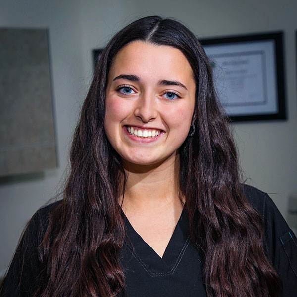 Smiling young woman with long dark hair wearing a black top, indoors, looking at the camera.